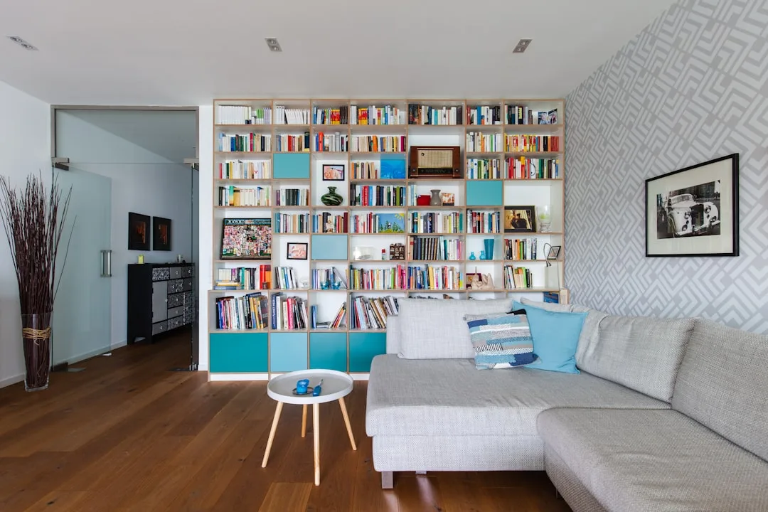 Floor-to-ceiling built-in bookcase wall with teal accents dividing living room space with gray sectional sofa