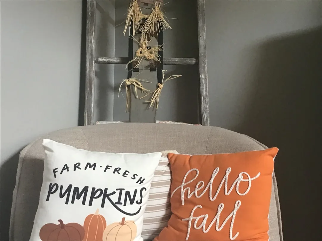 Budget fall decor pillows on chair with Farm Fresh Pumpkins and Hello Fall designs beside rustic ladder decoration
