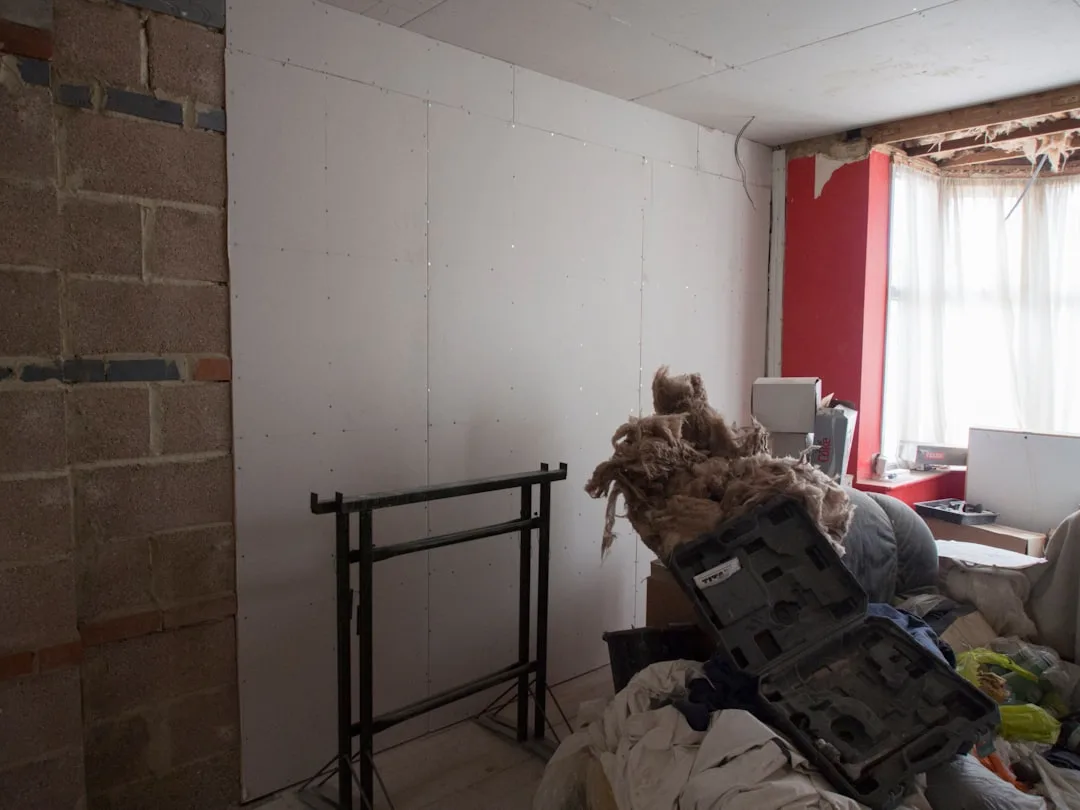 Room under renovation with drywall panels, exposed brick, insulation material and construction tools on floor