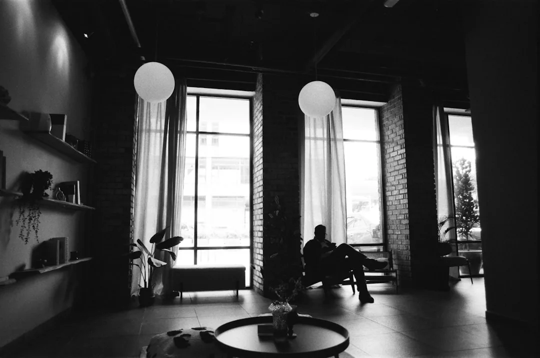 Person silhouetted in a moody black and white loft living space with tall windows, pendant lights, and brick walls