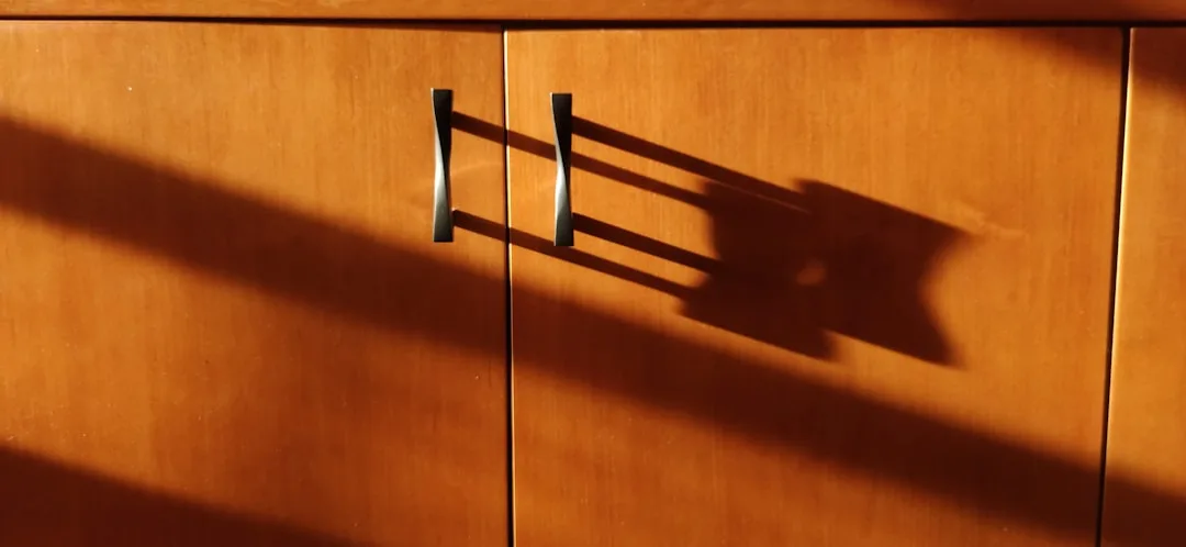 Warm wood kitchen cabinet doors with modern bar handles casting dramatic shadows in natural sunlight
