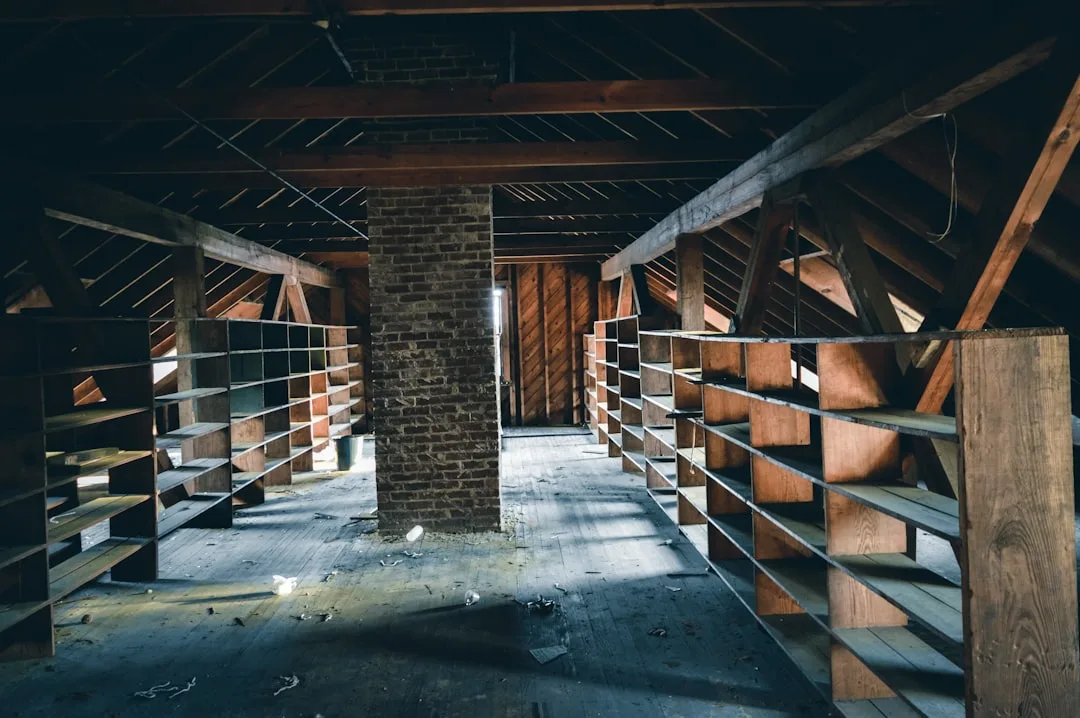 Abandoned attic space with exposed wooden rafters, empty shelving units, and unfinished wood plank flooring