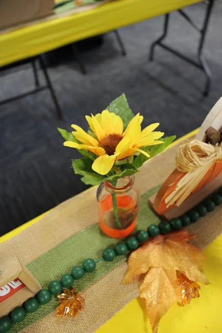 DIY dollar store fall centerpiece with sunflower in glass bottle, burlap runner, green beads, and autumn leaves