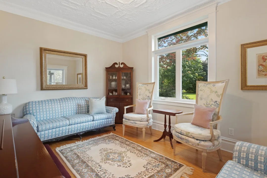 Classic rectangular living room with off-center window, blue sofa, floral armchairs, Oriental rug, and corner cabinet
