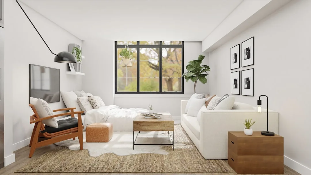 Studio apartment with white sofa, wood coffee table, and bed sharing one open living space with large black-frame window
