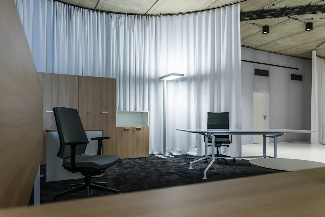 Ceiling-anchored curtain track dividing modern office space with white flowing curtains and ergonomic furniture