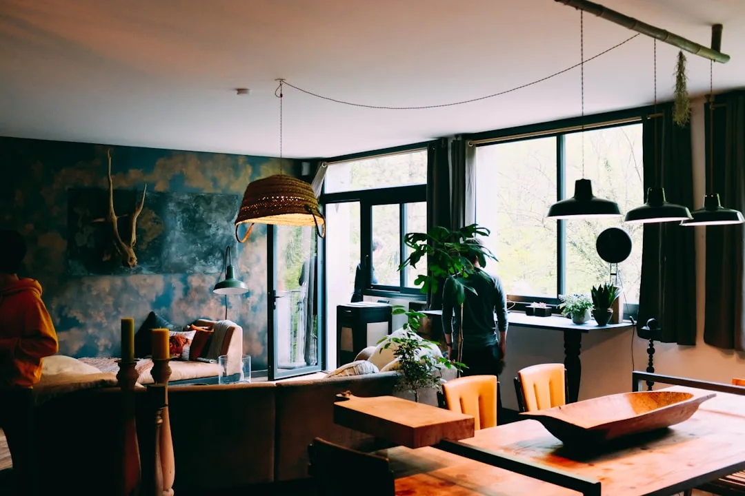 Eclectic DIY interior with textured blue wall, hanging wicker lamp, wooden dining table, and indoor plants in open livin