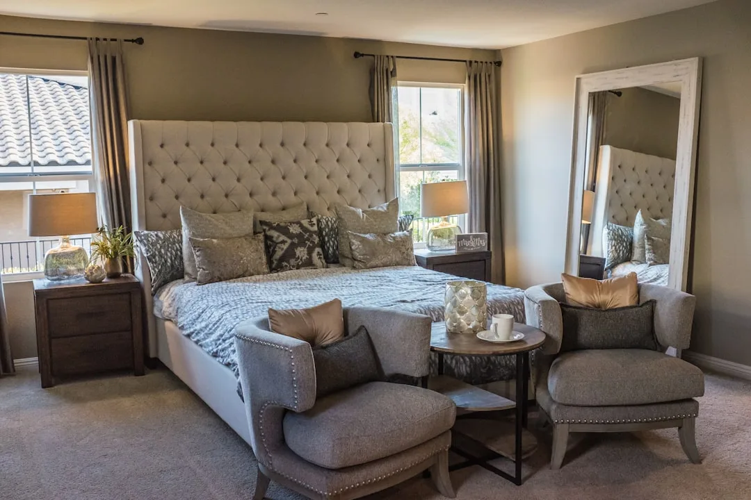 Master bedroom with tufted wingback bed, two gray accent chairs, and small side table showing functional furniture clear