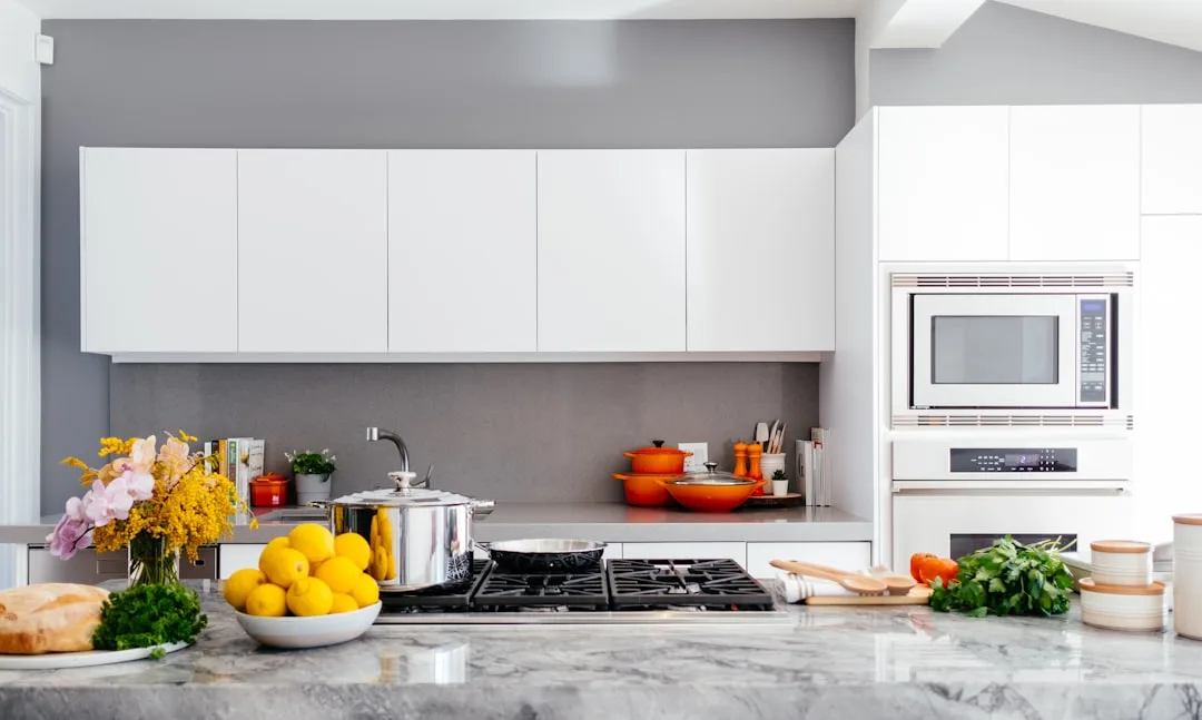 Modern white kitchen with marble countertop, gas cooktop, stainless steel pot, orange Le Creuset cookware, and built-in 