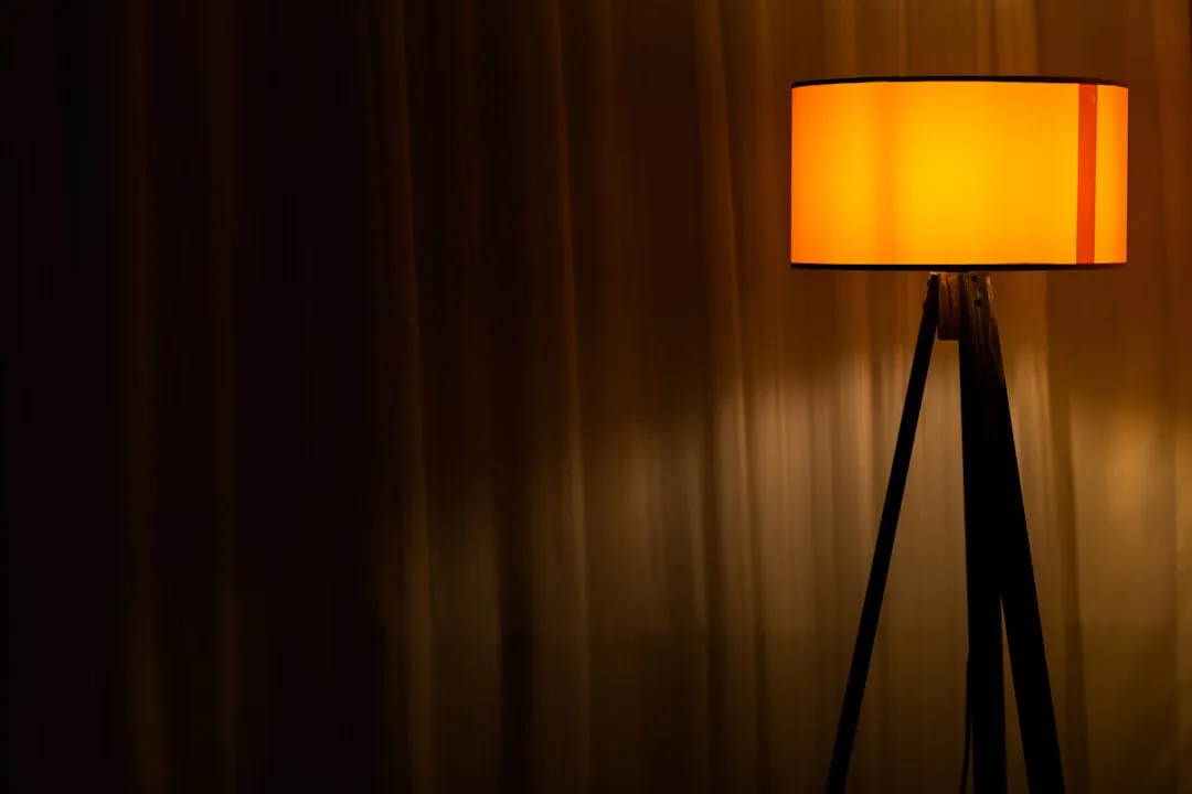 Warm orange glowing floor lamp on tripod stand against dark curtained background illustrating warm color temperature lig