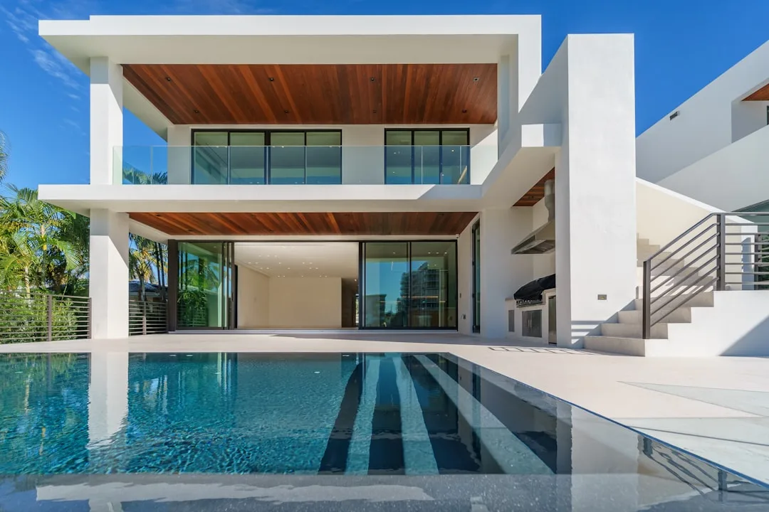 Contemporary luxury home with white flat roof, glass walls, wood ceiling accents, and infinity pool showcasing modern ar