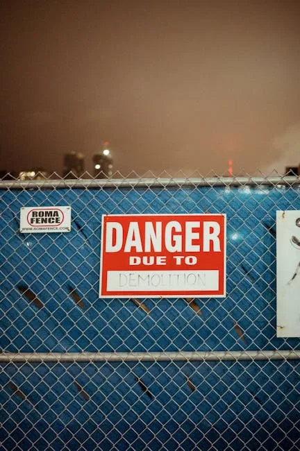 Red danger due to demolition warning sign on blue chain-link fence at construction site at night