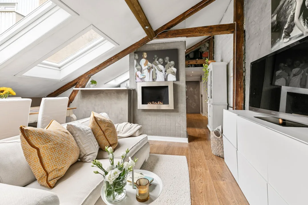 Attic living room conversion with exposed wooden beams, skylights, sloped ceilings, white sofa and modern fireplace