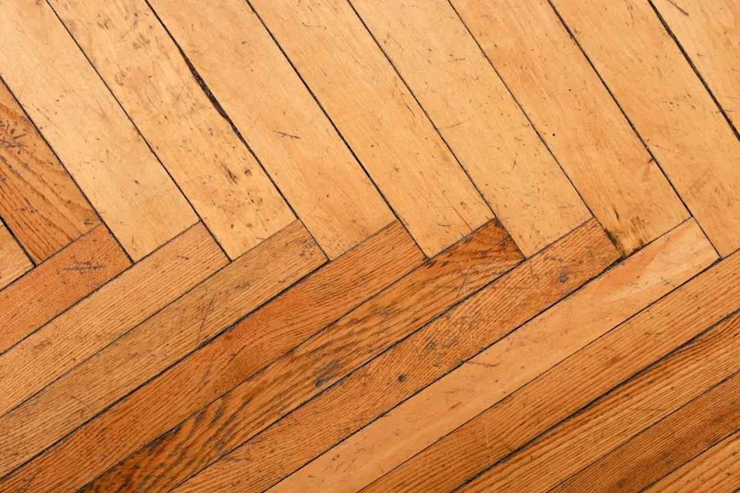 Herringbone hardwood parquet floor with visible scratches and wear showing DIY installation complexity and aging pattern