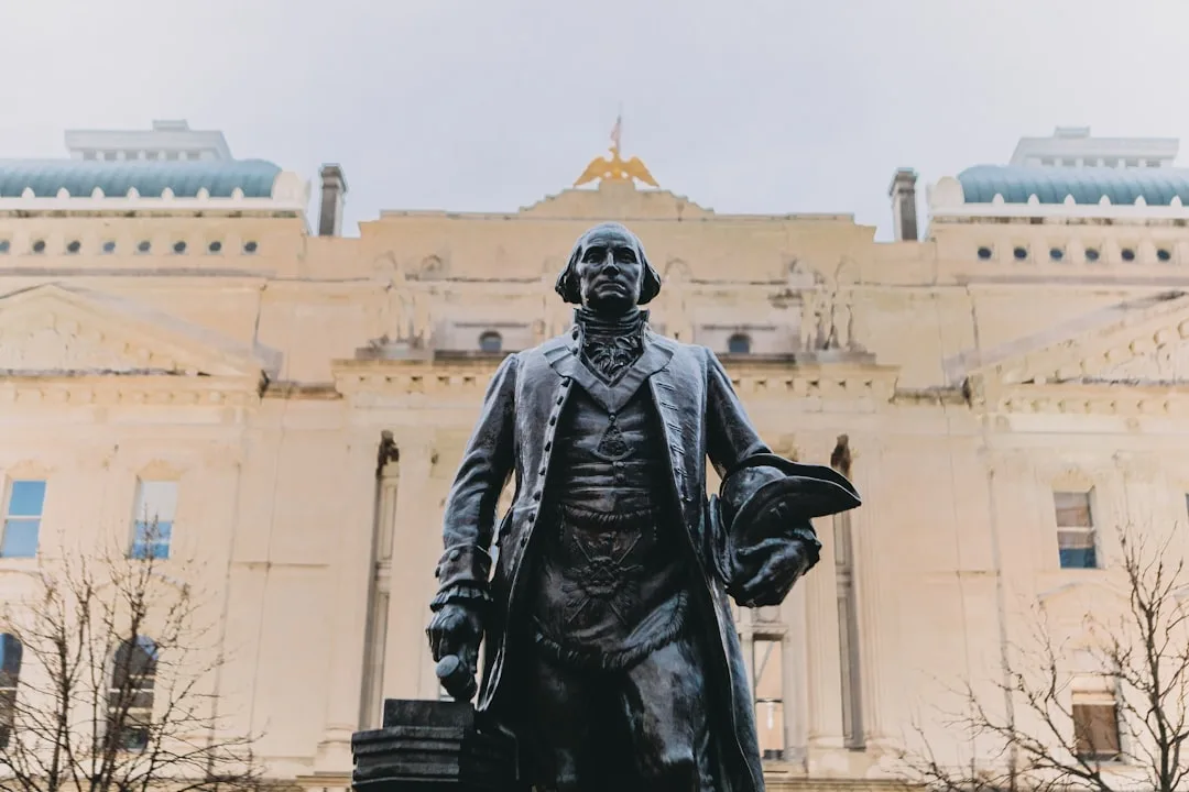 Bronze statue of a Founding Father in period coat holding tricorn hat before a neoclassical government building