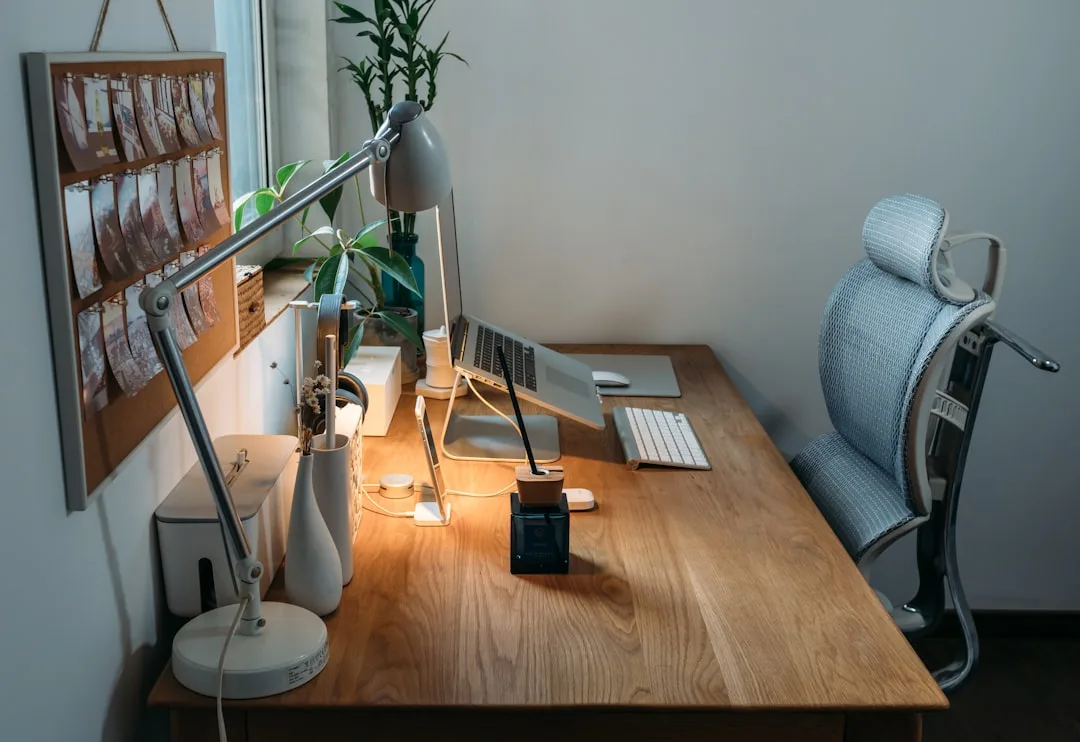 Ergonomic office chair at fixed-height wooden desk with laptop, keyboard, and desk lamp in home workspace
