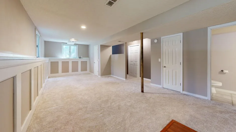 Finished basement with beige carpet, white wainscoting, recessed lighting, and open layout on a modest budget