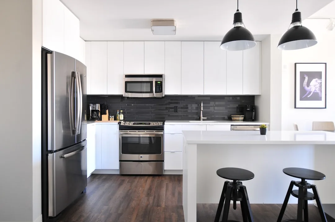 Modern renovated kitchen with white cabinets, stainless steel appliances, dark tile backsplash, and black pendant lights