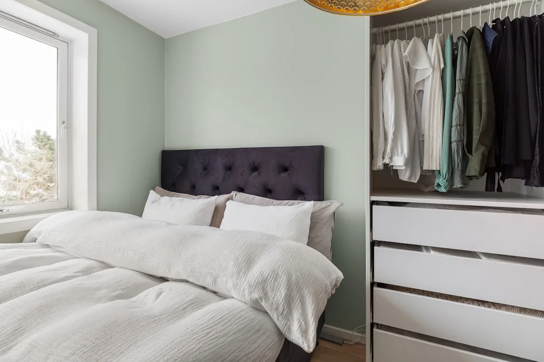 Bedroom with open wardrobe storage solution featuring hanging clothes and white chest of drawers beside a double bed