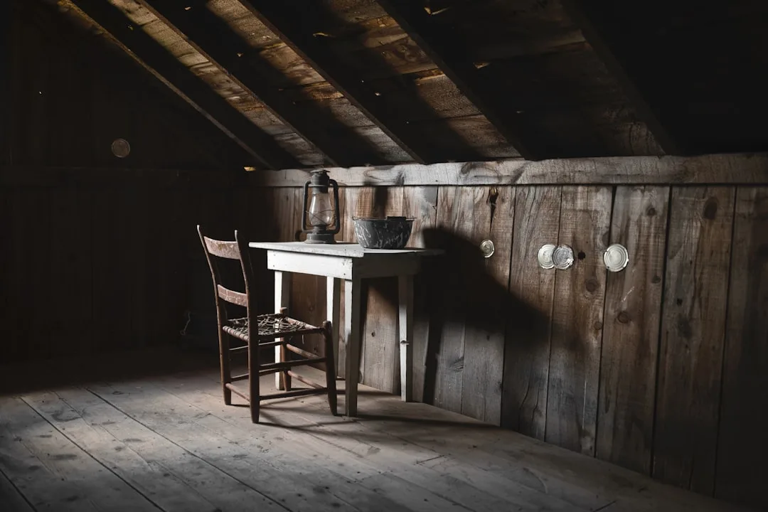 Rustic unfinished attic space with sloped wooden ceiling beams, plank floors, and vintage furniture