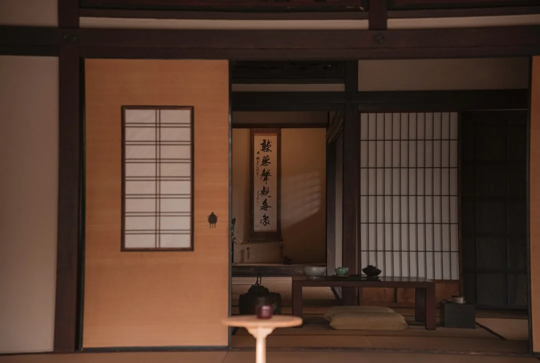 Traditional Japanese room with shoji screens, tatami mats, calligraphy scroll, and low wooden table in warm tones