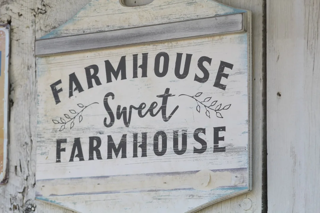 Rustic distressed wood farmhouse sign reading Farmhouse Sweet Farmhouse with whitewashed finish and decorative leaf deta