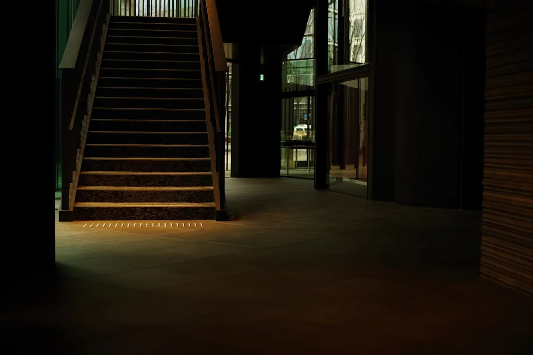 Floor-level LED lighting illuminating staircase base and hallway floor tiles in a dimly lit modern building interior