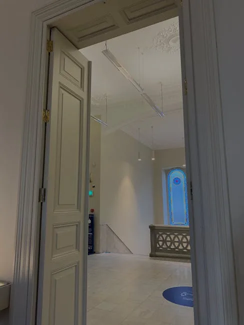 Elegant interior hallway with ornate plaster ceiling details, suspended lighting, and stained glass window visible throu