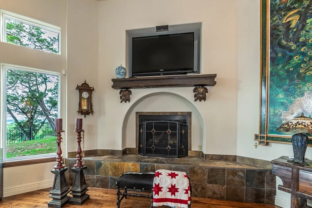 Fireplace with wall-mounted TV above mantel, arched hearth, slate tile surround, and large windows in living room