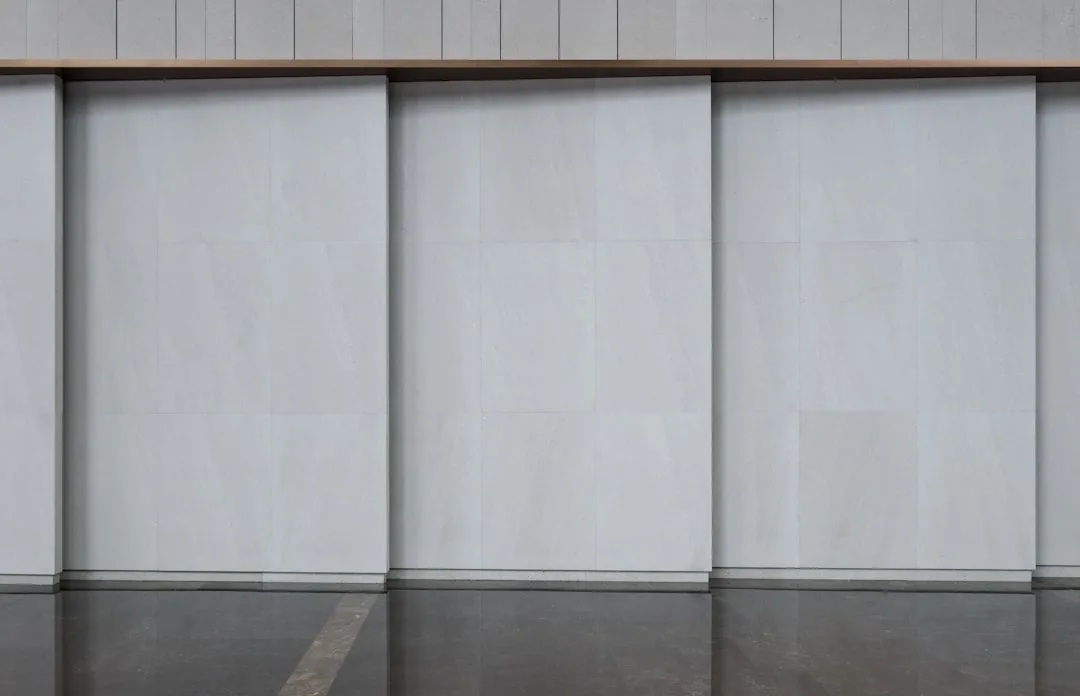 Large sliding stone panel wall dividers on a modern building exterior with reflective floor