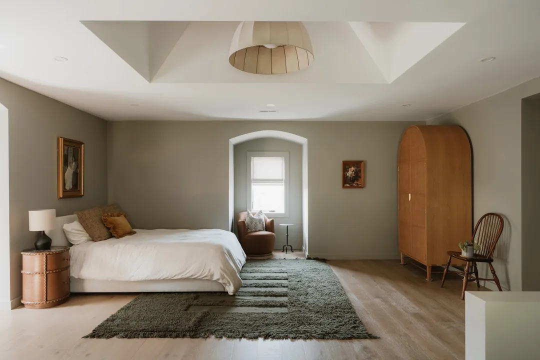 Bedroom with green shag rug placed in front of and partially under a white bed on light hardwood floors