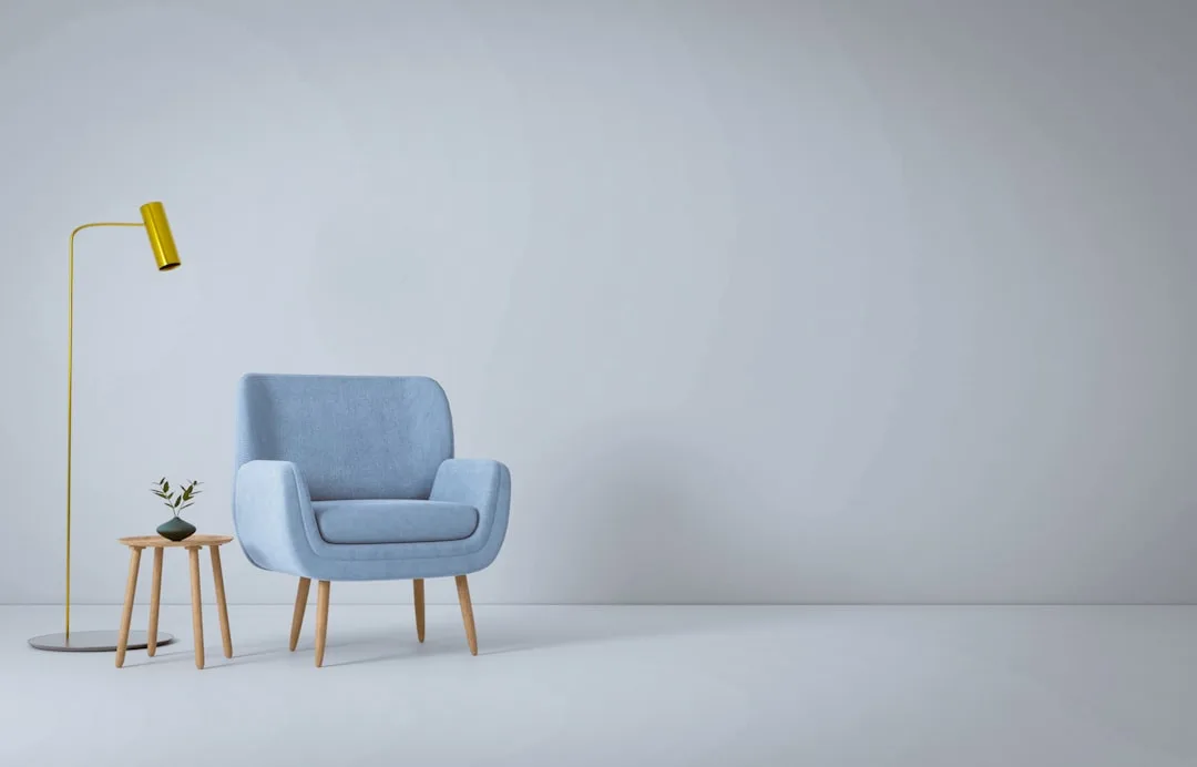 Neutral interior design with light blue armchair, yellow floor lamp, and wood side table against a soft gray wall