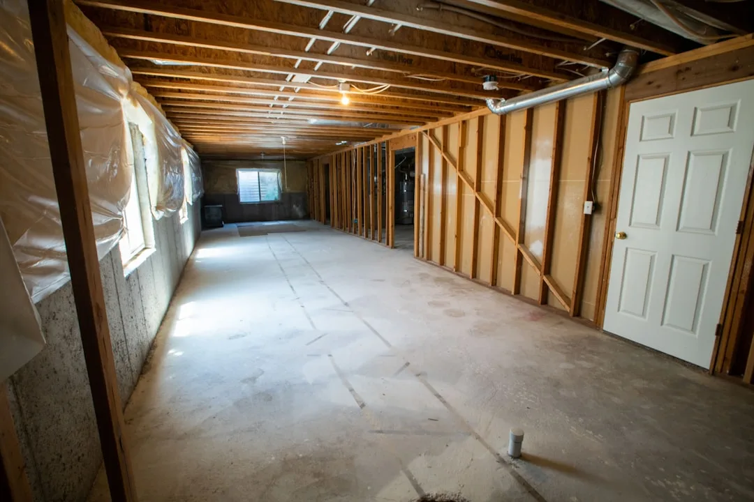 Unfinished basement with exposed wood framing, concrete floor, plastic vapor barrier walls, and HVAC ductwork