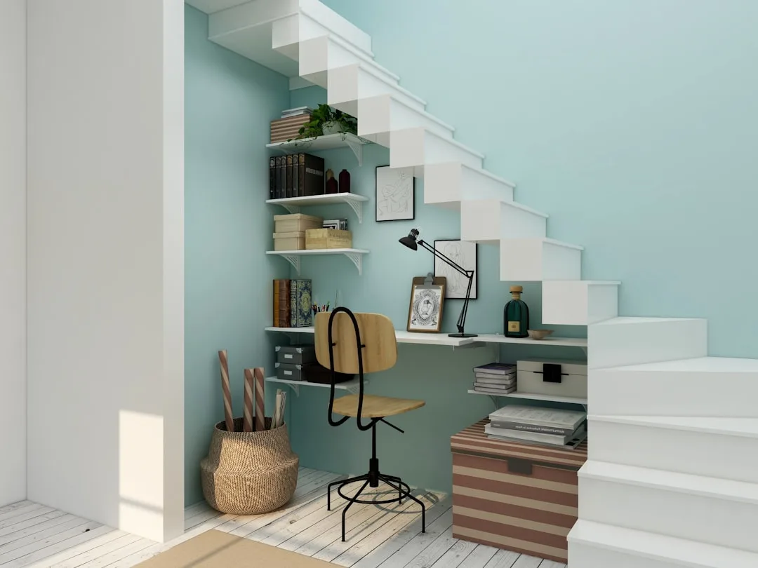 Compact under-stair home office nook with wooden chair, wall-mounted shelves, desk lamp, and teal accent wall