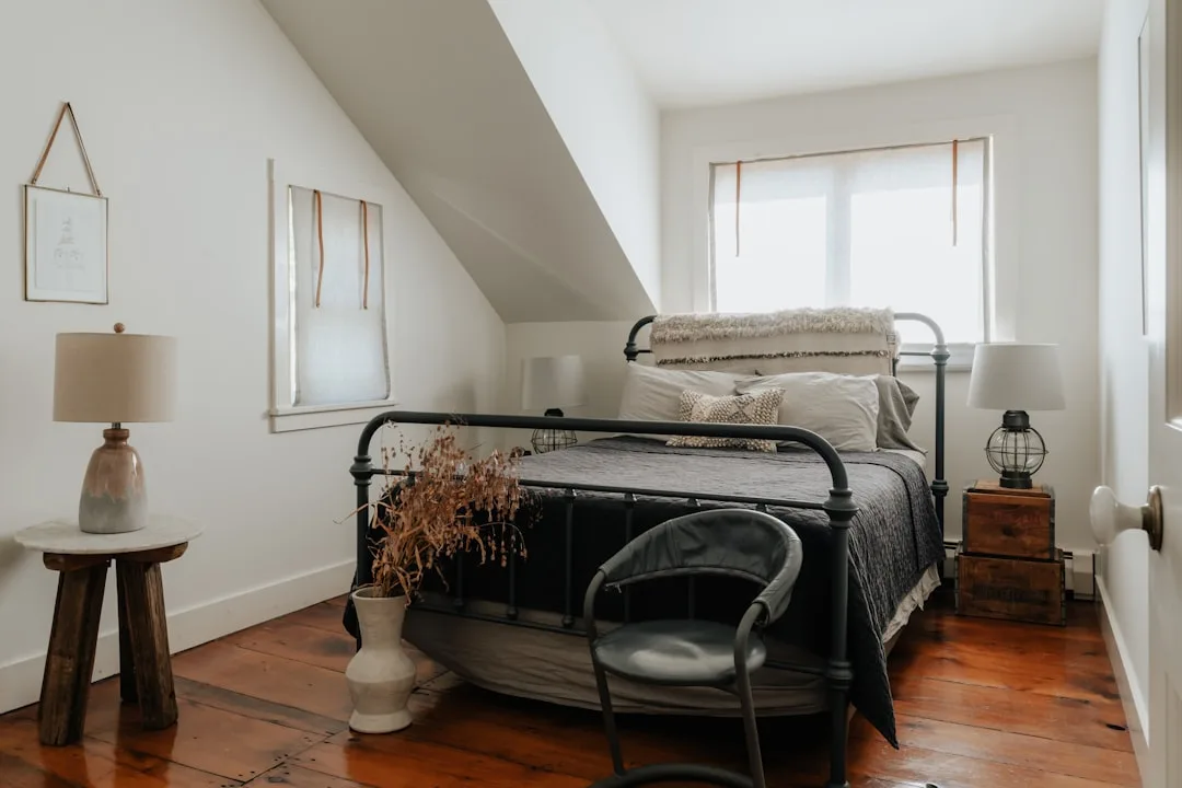 Cozy attic bedroom conversion with sloped ceiling, black iron bed frame, hardwood floors, and natural light from window