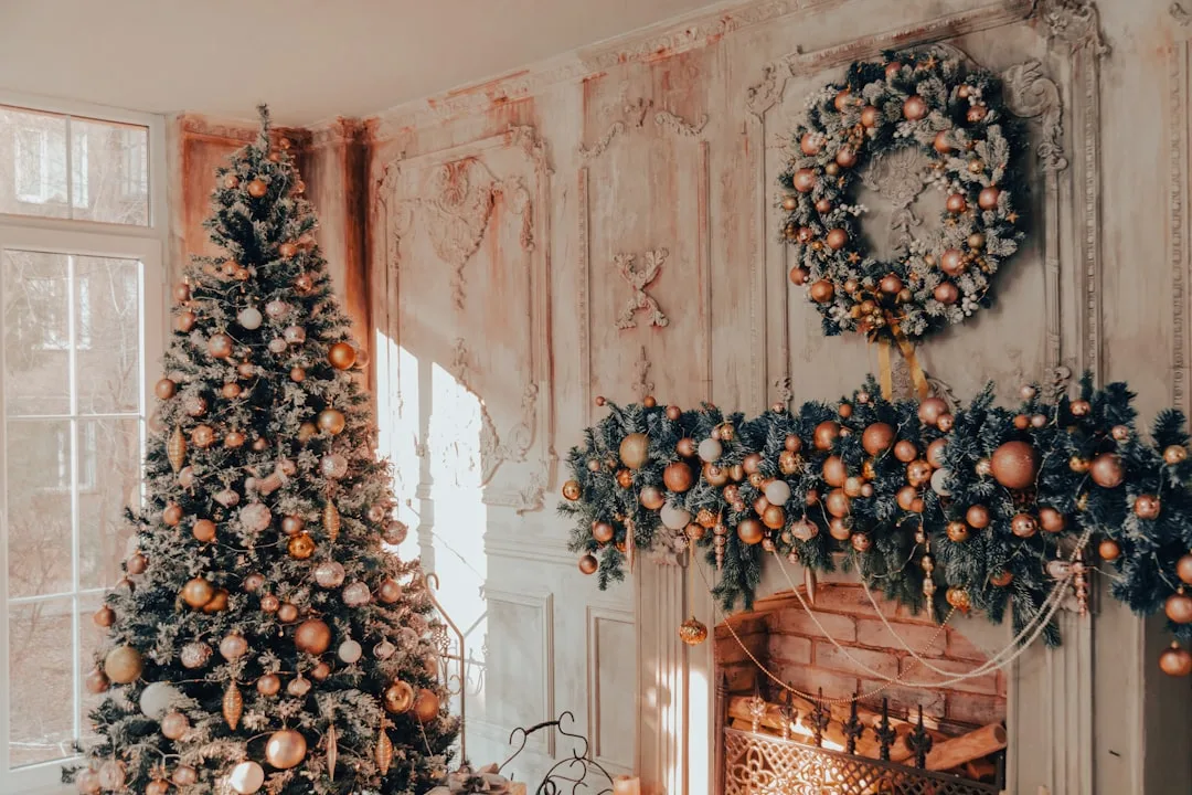 Christmas tree with gold ornaments beside fireplace with wreath and garland in elegant apartment living room