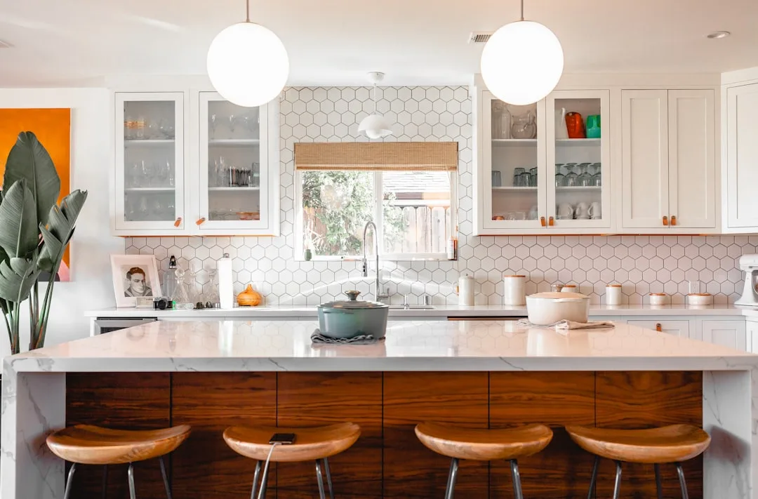 Modern kitchen with marble countertop island, white matte cabinets, and warm wood accents showing mixed finish design