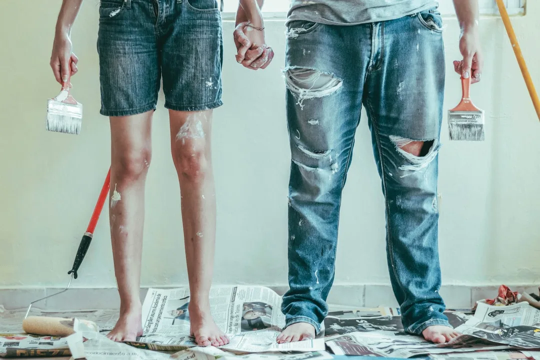 Couple holding hands while painting walls during DIY home renovation, holding paint brushes with paint-splattered clothe