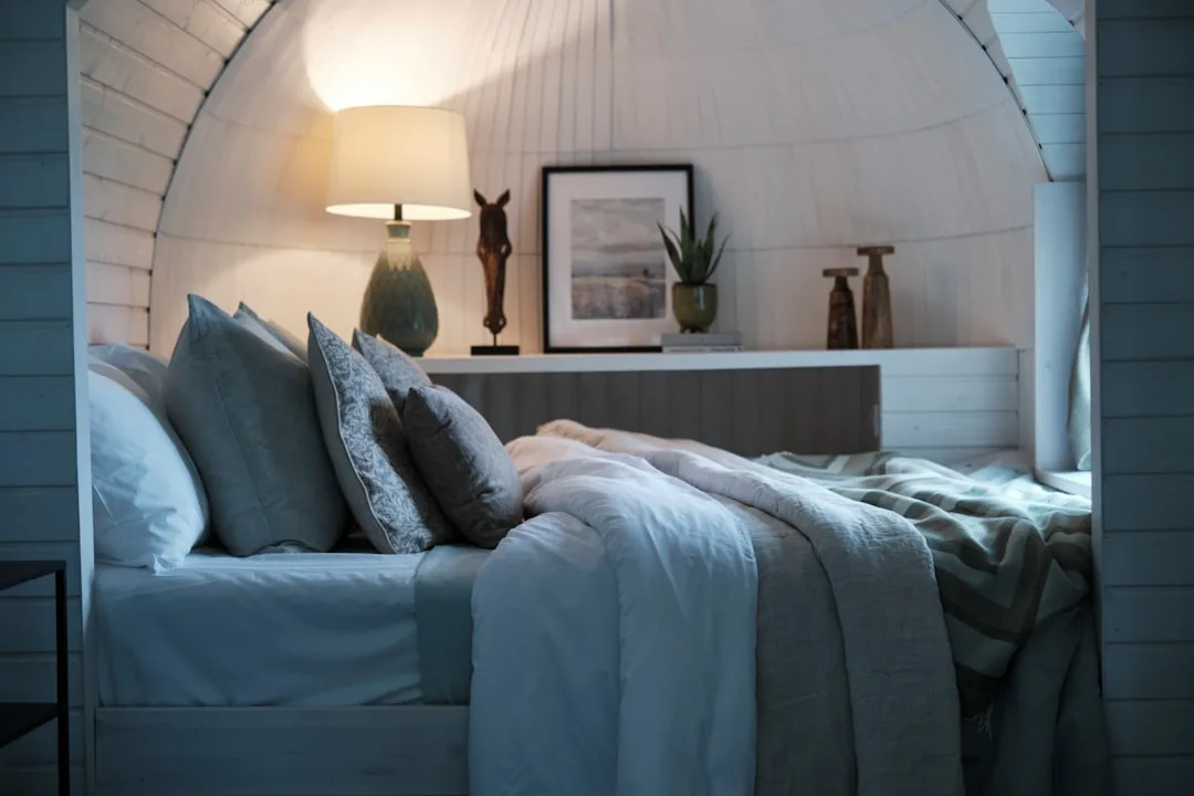 Cozy small bedroom with arched alcove bed, lamp on shelf nightstand alternative, layered gray and white bedding