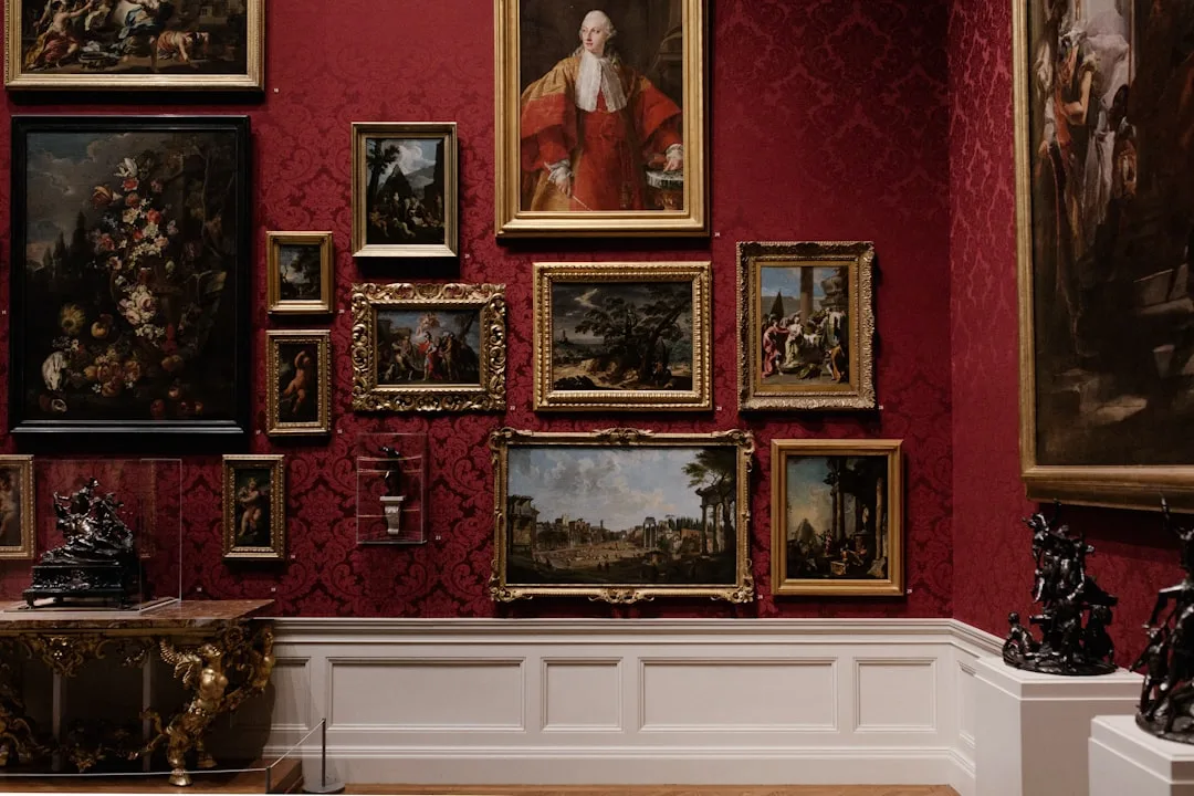 Classic gallery wall with gold-framed paintings arranged on deep red damask wallpaper in an elegant museum room