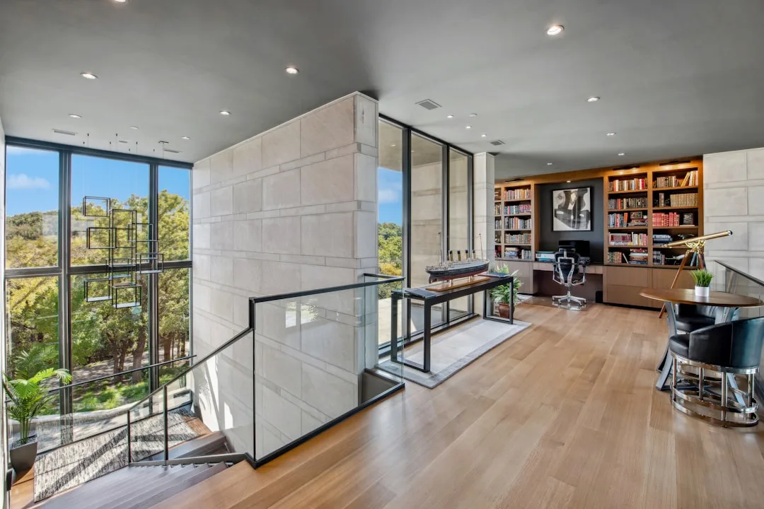 Contemporary mansion upper floor with floor-to-ceiling glass walls blending indoor living space with outdoor tree views
