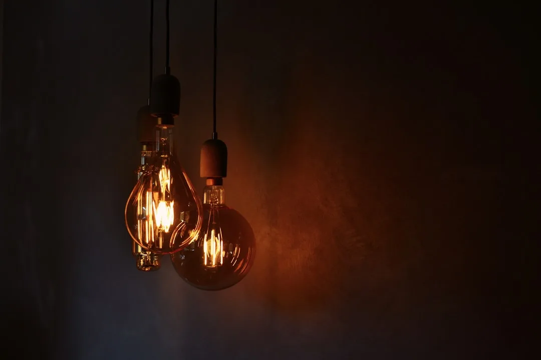 Two vintage Edison filament pendant bulbs glowing warm amber light against dark wall in moody interior setting