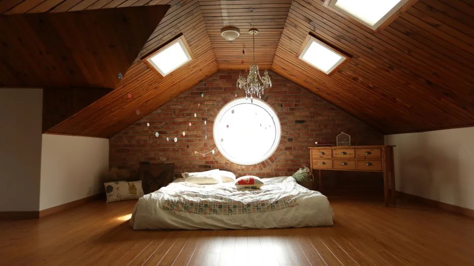 Finished attic bedroom conversion with vaulted wood ceiling, skylights, round brick window, and low platform bed