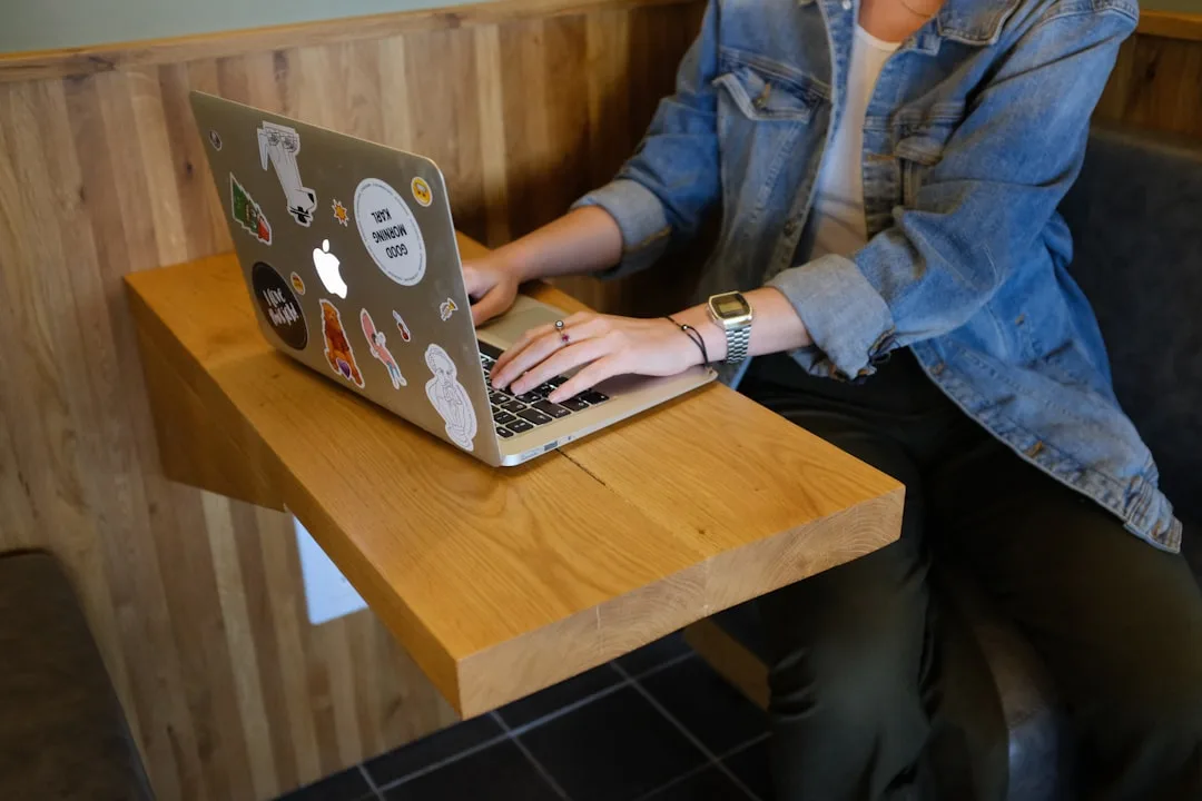 Person using MacBook laptop on a wooden floating wall-mounted desk in a cafe setting