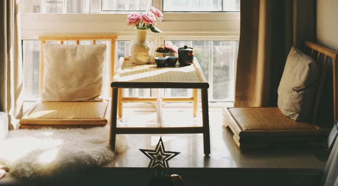 Japandi-style window nook with low wooden table, floor cushions, tea set, and pink roses in warm natural light