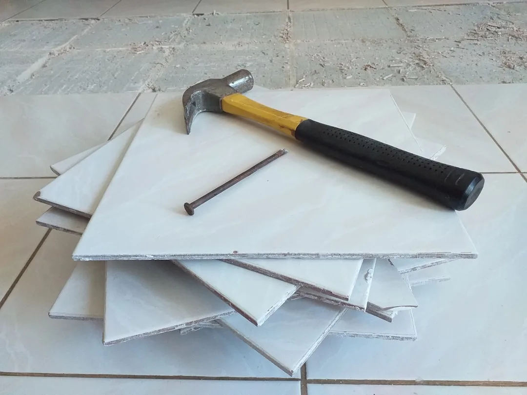 Stack of white ceramic floor tiles with claw hammer and nail for DIY renovation budget planning