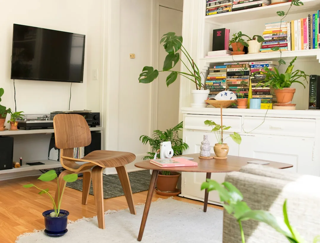 Mid-century modern Eames chair and wood coffee table in a small apartment living room with bookshelves and houseplants