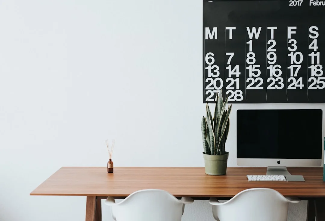 Freestanding wooden desk with iMac, plant, and calendar above in a minimalist home office setup