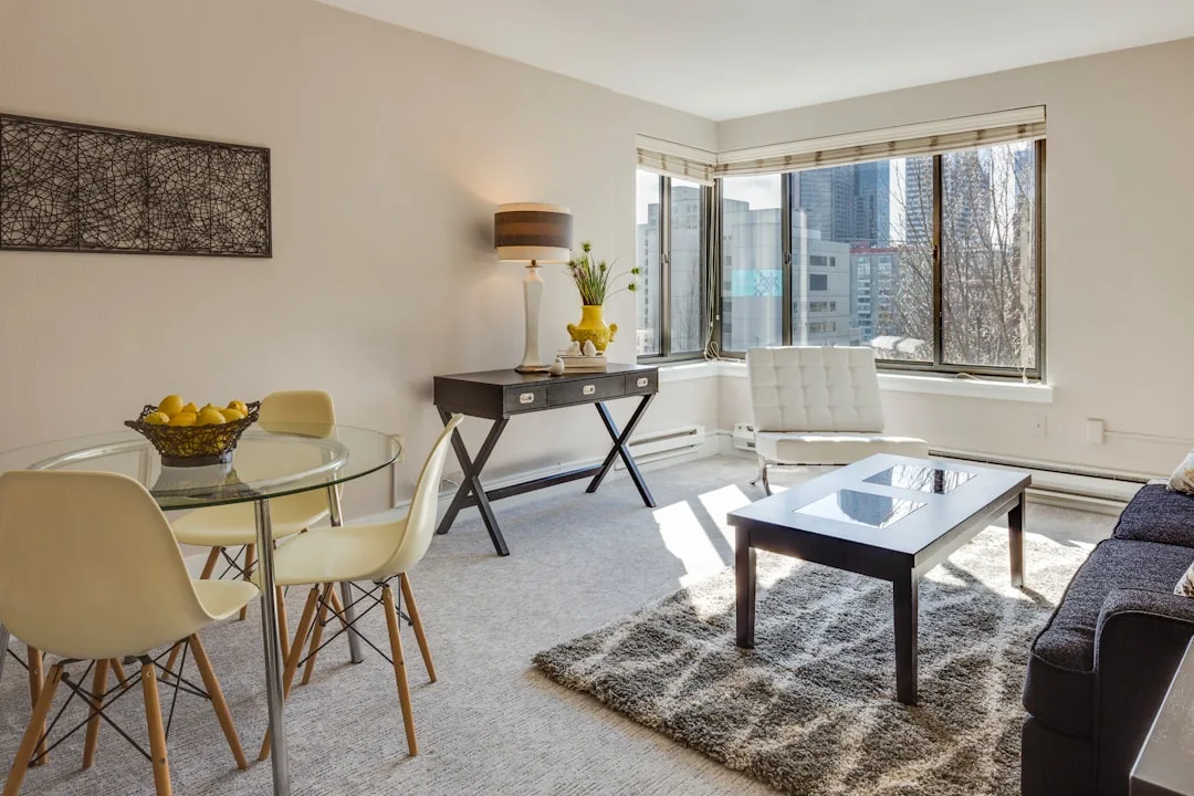 Small apartment living and dining area with glass table, Eames chairs, and city view window showing open floor plan