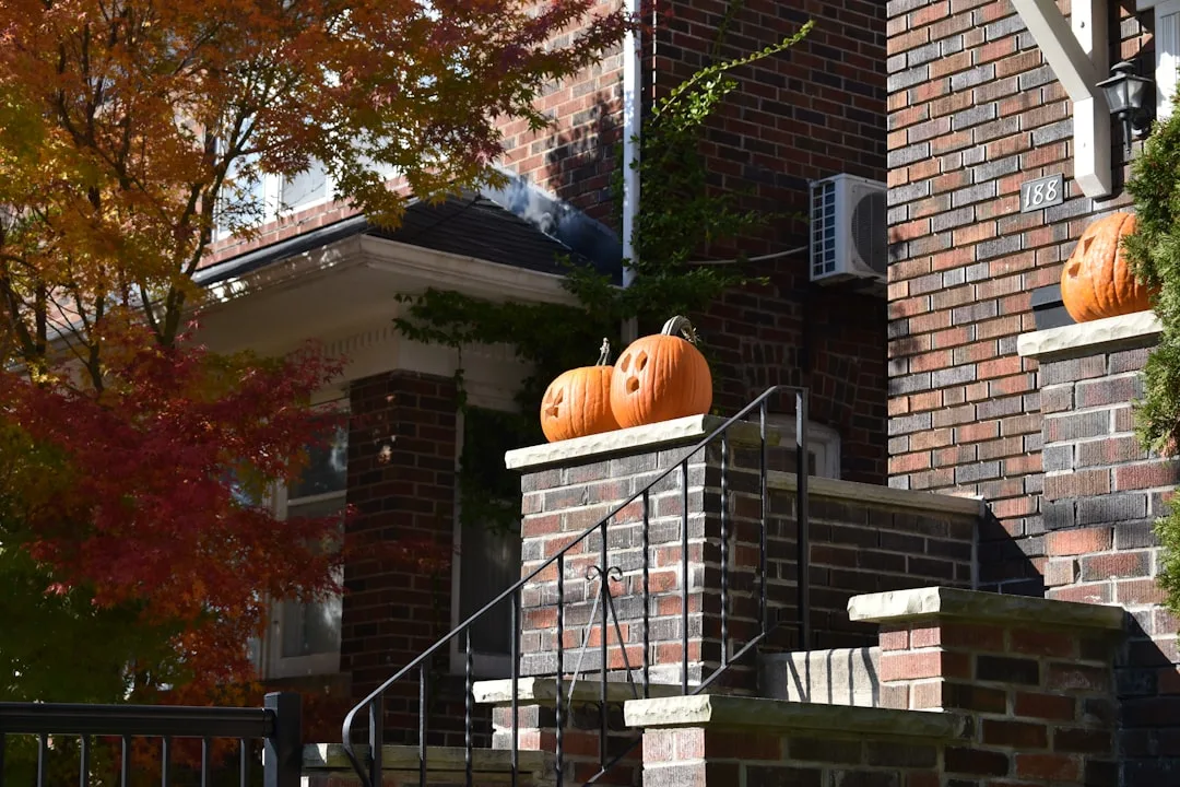 Carved jack-o-lantern pumpkins decorating brick front porch steps of a house in autumn fall season